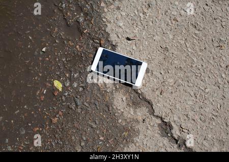 Mobile phone lying on pavement in puddle. Stock Photo