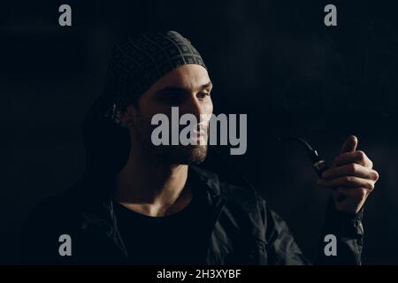 Man smoking a pipe on dark background. Back lit profile portrait. Stock Photo