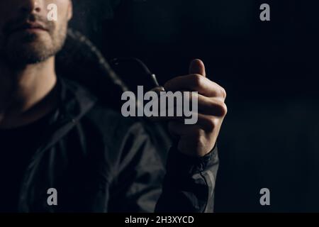 Man smoking a pipe on dark background. Back lit profile portrait. Stock Photo