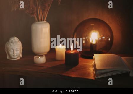 Round mirror on wooden shelf with two burning candles and small porcelain Buddha head Stock Photo