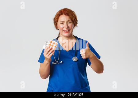 Medicine, healthcare and coronavirus concept. Smiling redhead female doctor, physician showing thumbs-up as advice treatment fro Stock Photo