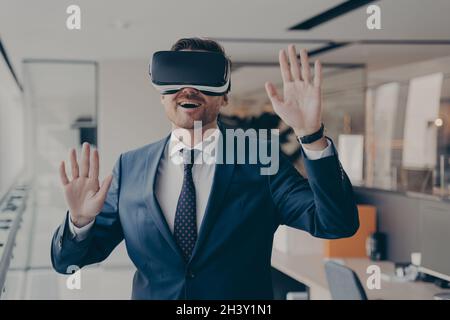 Young excited businessman dressed formally using virtual reality headset while working in office Stock Photo