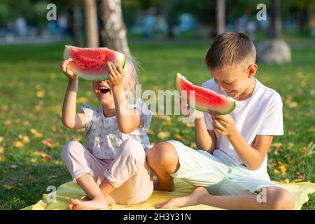 To cute kids lttle boy and girl eating juicy watermelon in the picnic at autumn park meadow Stock Photo