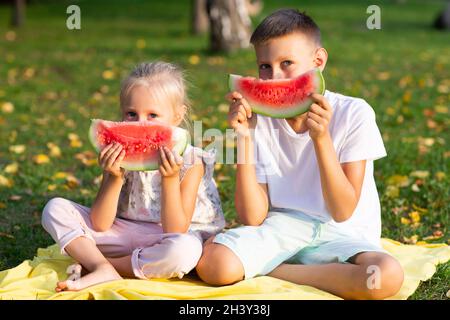 To cute kids lttle boy and girl eating juicy watermelon in the autumn park meadow Stock Photo