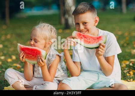 To cute kids lttle boy and girl eating juicy watermelon in the autumn park meadow Stock Photo