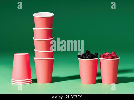Fresh berries in red cup on green background and set of disposable paper cups Stock Photo