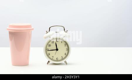 Round retro alarm clock and pink ceramic cup with coffee on white table Stock Photo