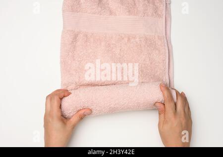 Female hand holds a pink terry towel on a white table, top view Stock Photo