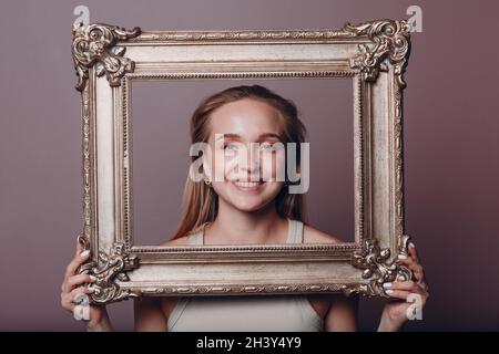 Millenial young woman blonde hair holds gilded picture frame in hands face portrait Stock Photo