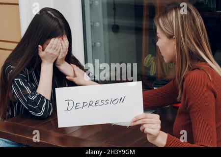 Hidden depression concept. Woman crying. Second woman holding white sheet paper labeled word Depression in hand. Two women talki Stock Photo