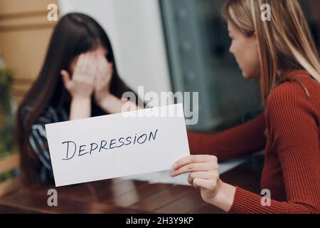 Hidden depression and stress concept. Woman crying. Second woman holding white sheet paper labeled word Depression in hand Stock Photo