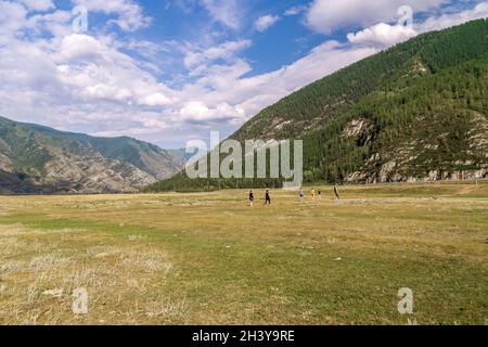 People walk from rock paintings of Kalbak-Tash tract past Chuisky Deer Stone to the Chuisky tract in valley between mountains overgrown with coniferou Stock Photo