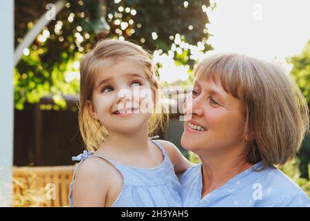 Loving middle-aged grandma holding smiling cute girl granddaughter while standing in garden Stock Photo
