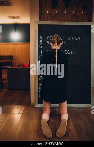 Young woman writing cafe menu on black desk chalkboard using chalk. Stock Photo
