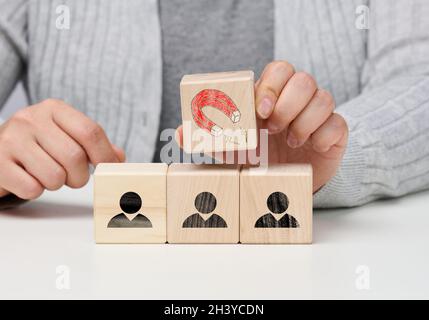 Female hand holds a wooden cube with a magnet over the cubes with little men, recruiting for a strong team. Open vacancies in th Stock Photo