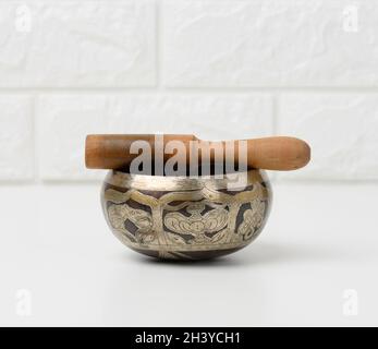 Tibetan singing copper bowl with a wooden clapper on a white wooden table, objects for meditation and alternative medicine Stock Photo