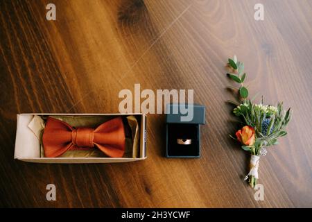 Accessories for the groom bow tie, gold wedding ring and boutonniere on a wooden floor in a row. Stock Photo