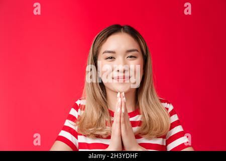 Thankful cute happy asian girl bowing politely show namaste gesture gladful. Joyful attractive blonde hold hands pray appreciate Stock Photo