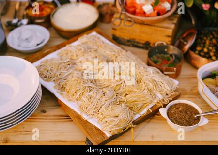 Spaghetti on a wooden plank for cutting with cooked meals and clean plates. Stock Photo