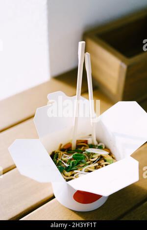 Noodles with pork and vegetables in take-out box on wooden table. Stock Photo