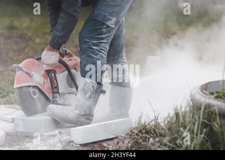 Worker mason cuts the sidewalk tile with circular saw while repairing sidewalk in city street Stock Photo