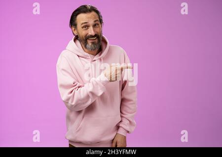 Friendly carefree caucasian bearded man in pink hoodie pointing right intoducing family members smiling proudly delighted showin Stock Photo