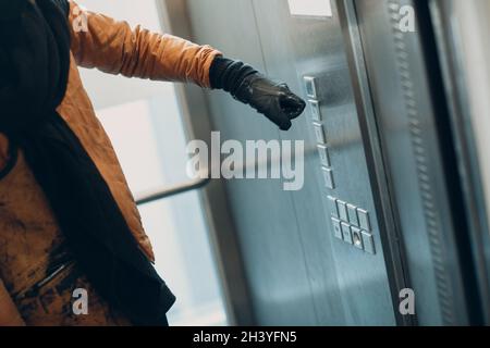 Close up of hand in glove forefinger pressing the button elevator during coronavirus pandemic covid-19 quarantine concept Stock Photo