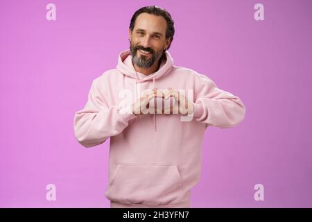 Family in heart. Portrait lovely handsome romantic bearded man in pink hoodie passionatly looking camera show love gesture smili Stock Photo