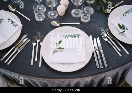 Wedding dinner table reception. White round plates on a round table with gray tablecloth, white Chiavari chairs with white pillo Stock Photo