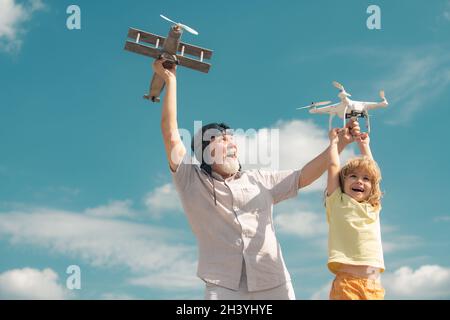 Grandson child and grandfather playing with toy plane and quadcopter drone against sky. Child pilot aviator with plane dreams of traveling. Family Stock Photo