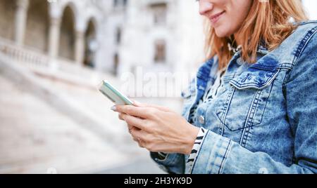 Young redhead Caucasian woman messaging on smartphone in city closeup Stock Photo