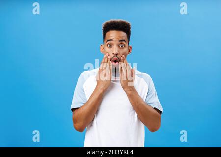 Attractive young dark-skinned guy likes hearing fresh rumors learning new hot details gasping opening mouth holding hands on fac Stock Photo