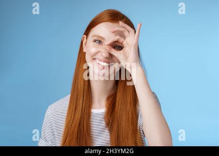 Charismatic happy adorable redhead teenage girl sincere eyes making circle eye show okay ok sign delighted like approve cool ide Stock Photo