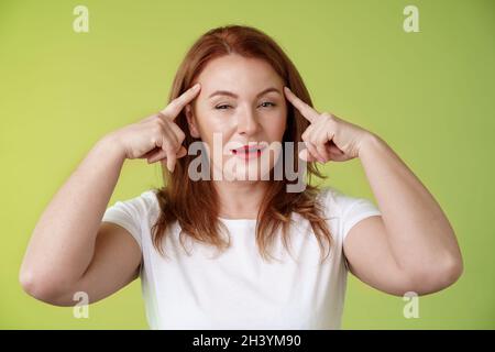 Smart choice. Intrigued thoughtful good-looking assertive redhead creative middle-aged woman touch temples squinting pondering i Stock Photo