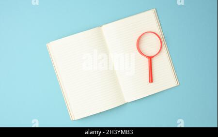 Paper notebook with blank white sheets and a red magnifier on a blue background. Background for inscriptions Stock Photo