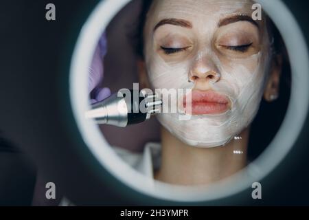 Young woman receiving electric RF lifting facial massage at beauty spa with electroporation equipment. Stock Photo