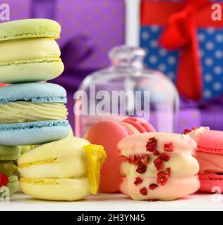 Baked macarons with different flavors and rosebuds on a white background, behind gift boxes Stock Photo