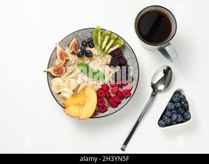 Cup of coffee and boiled oatmeal with fruits in a round plate on a white table, top view. Stock Photo