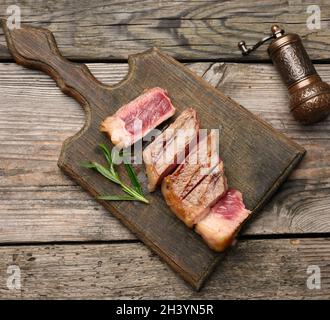 Sliced fried beef steak New York striploin on a wooden cutting board, degree of doneness rare Stock Photo