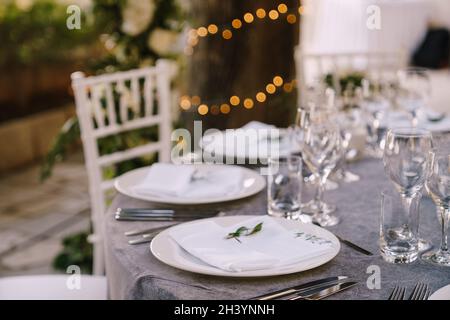 Wedding dinner table reception. White round plates on a round table with gray tablecloth, white Chiavari chairs with white pillo Stock Photo