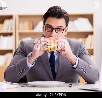 Hungry funny businessman eating junk food sandwich Stock Photo