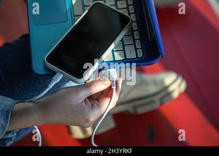 The smartphone is connected to the laptop via USB cable. Stock Photo