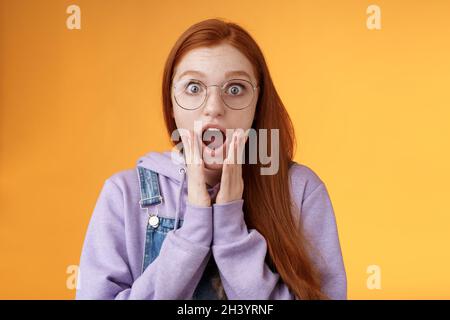 Shocked impressed redhead girlfriend drop jaw gasping screaming wow omg touch cheek near mouth wide eyes surprised reacting asto Stock Photo