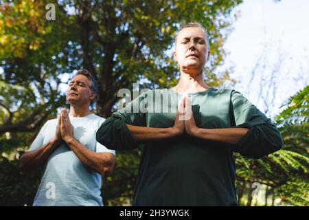 Peaceful senior caucasian couple practicing yoga, meditating in sunny garden Stock Photo