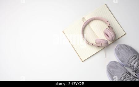 Pink wireless headphones, a pair of sneakers and a notepad on a white background, top view. Womens clothing Stock Photo