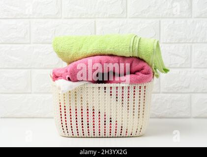 Clean rolled terry towels in a plastic basket on a white shelf, bathroom interior Stock Photo