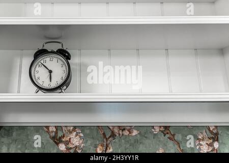Classic vintage alarm clock on the shelf in the interior of the room. Stock Photo