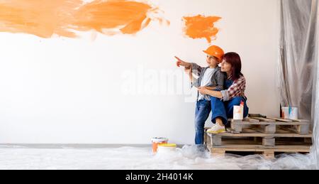 Mom and son are doing repairs in a new home. painted the wall orange. wall in the apartments with space for text. Loving mother hugging her son Stock Photo