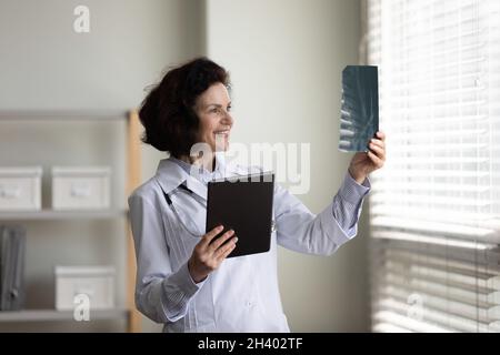 Happy middle aged female surgeon analyzing x-ray images. Stock Photo