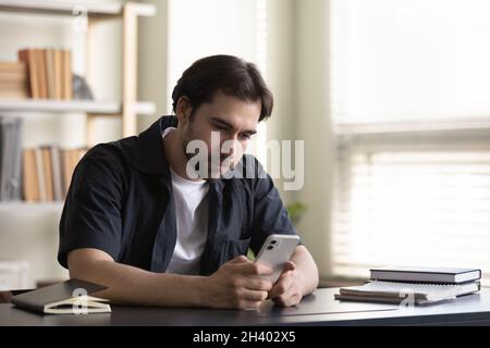 Happy young 30s man using cellphone sitting at table. Stock Photo